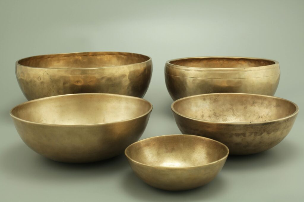 Five antique brass singing bowls on a neutral gray background, creating a serene atmosphere.